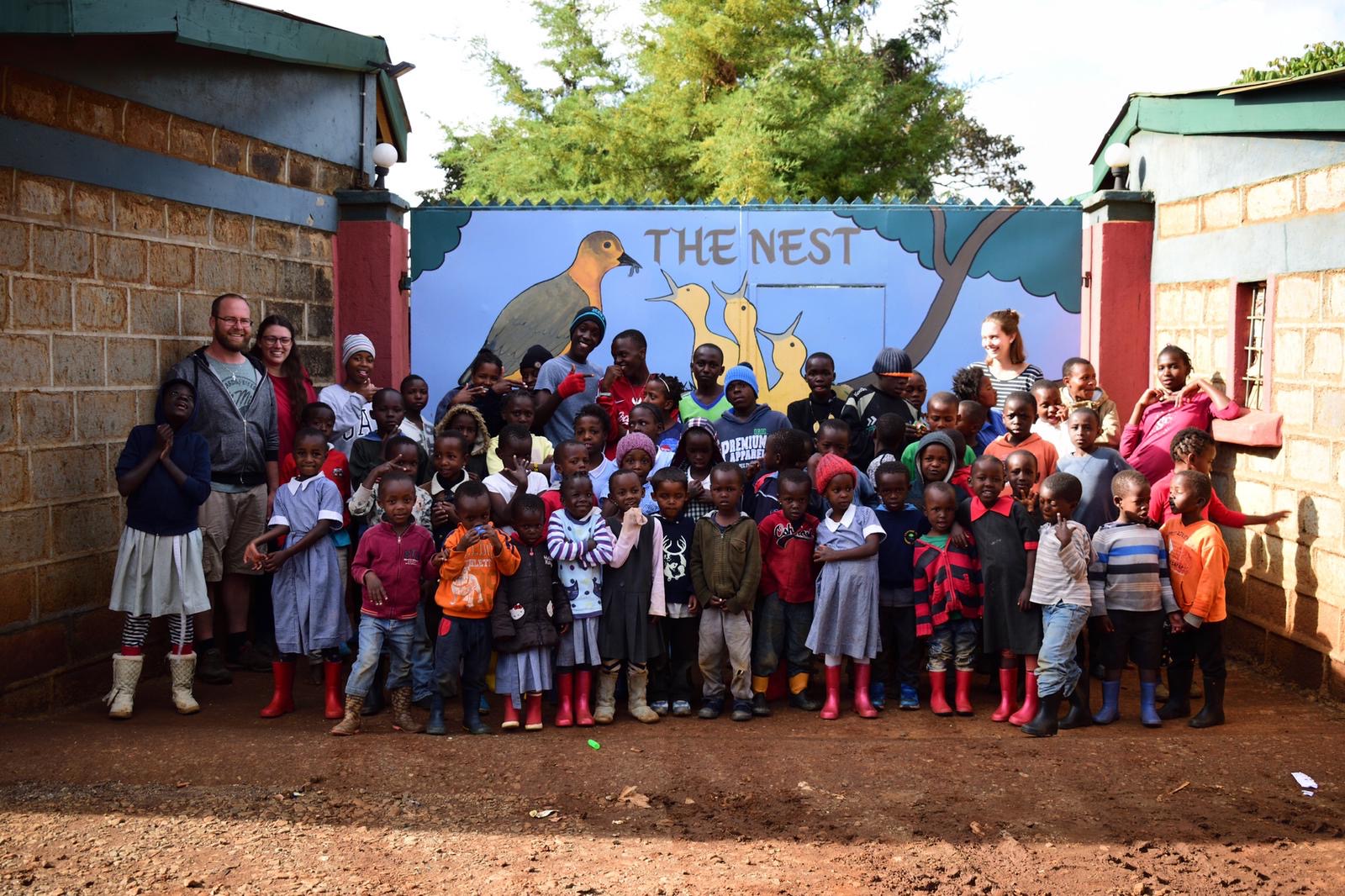 Kinder und Betreuer:innen des The Nest vor dem bemalten Eingangstor des Kinderheims in Limuru